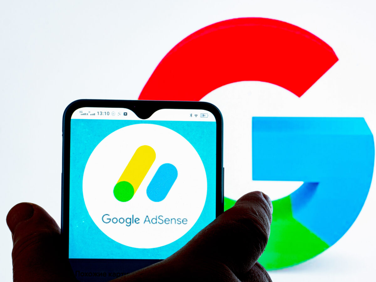 In this photo illustration Google AdSense logo seen displayed on a smartphone and Google logo in the background.